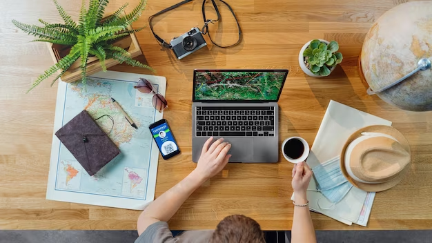 Man using a laptop with a table featuring a map, hat, camera, and a globe.